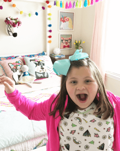 Image of a little girl with a happy excited face while standing in front of a canopy bed.