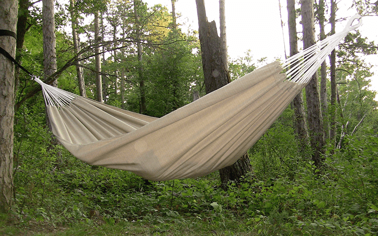 A cream colored hammock that is tied up on a tree.