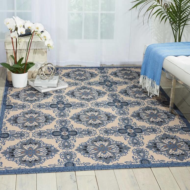 Vintage and blue patterned outdoor rug in a sun room with a planter on the side and a bench on the opposite side. 