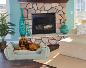 A dog on a dog bed in a living room in front of a fire place with two vases on the side.