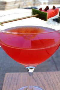 Photograph of a red cocktail with a watermelon on the cup.