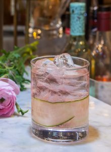 Image of a cocktail in a small short glass with a blush color to is and ice at the top of the drink.