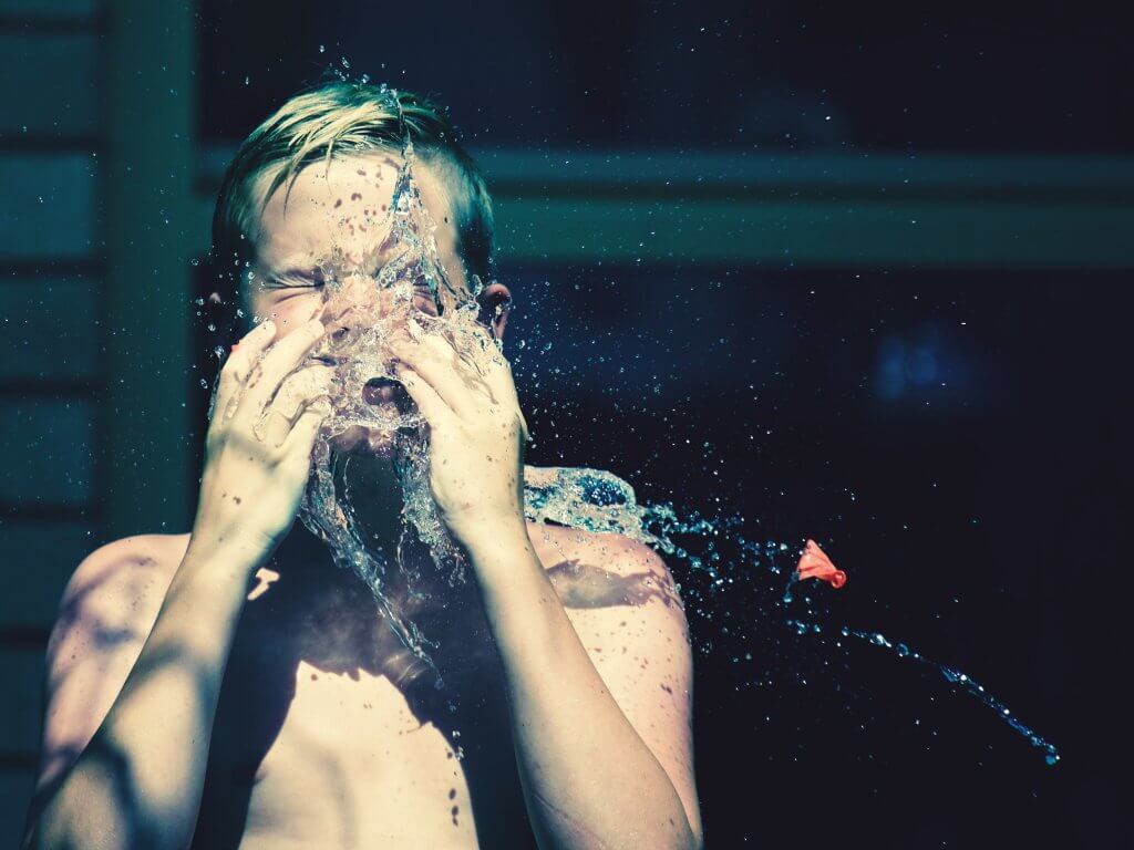 boy with eyes closed getting hit with water froma water balloon