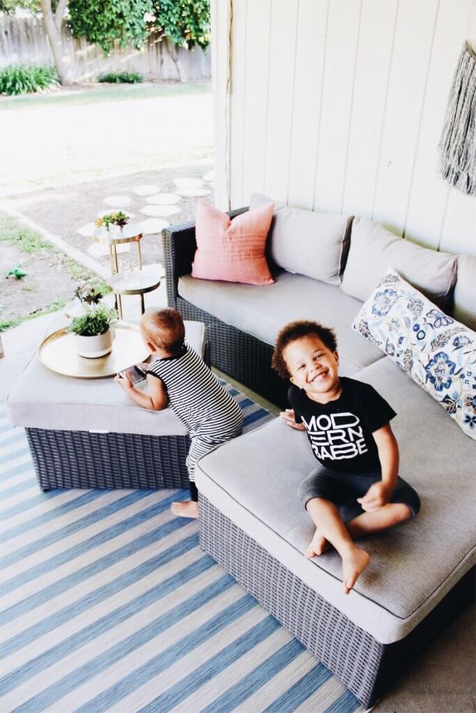 kid sitting on an outdoor sofa with another kid standing by the matching table