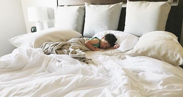 child sleeping on bed with white sheets
