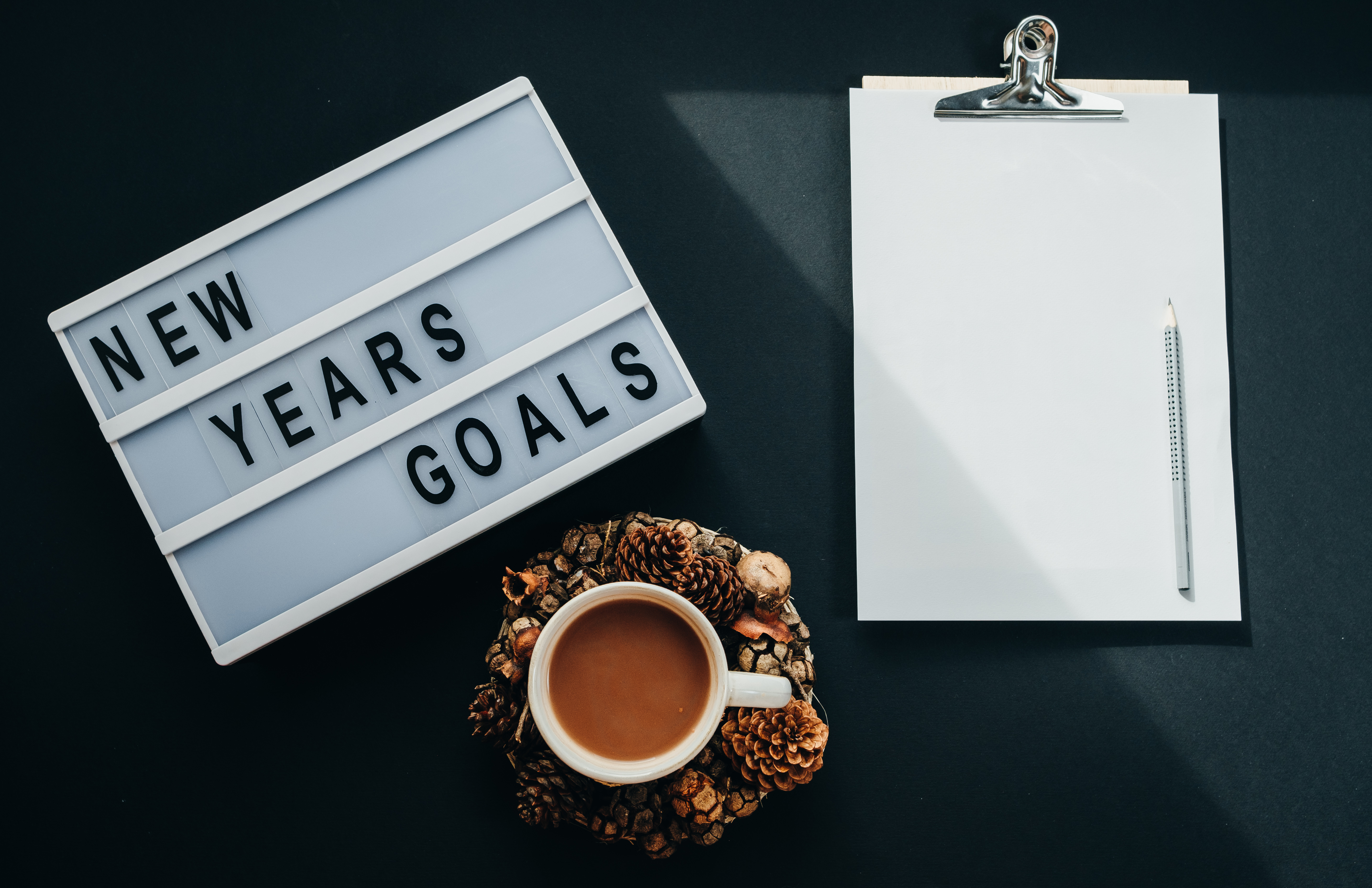 Hot cocoa, Board with "GOALS" text, notebook, pencil on black background, top view, flat lay