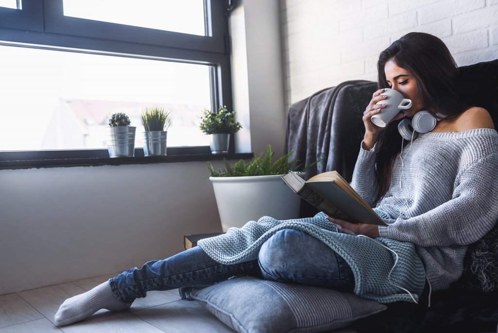 Beautiful young woman at home drinking coffee reading a book