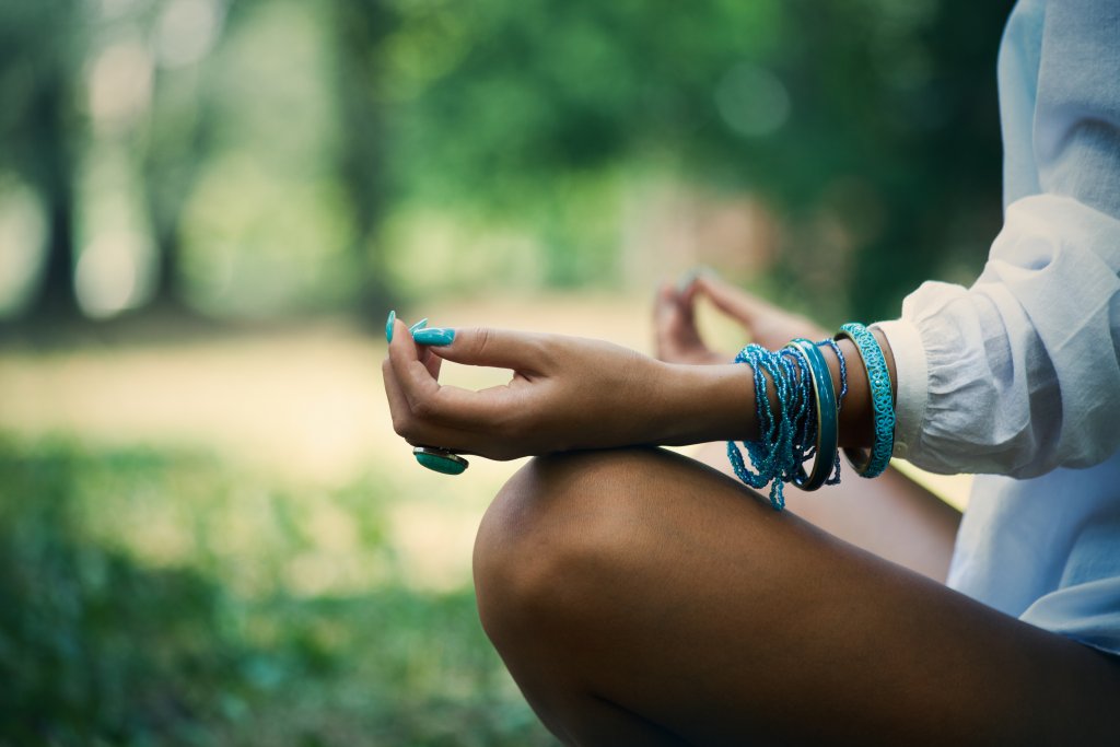 woman meditate in wood, close up of legs, hands and part of body in white shirt, selective focus on hand, side view