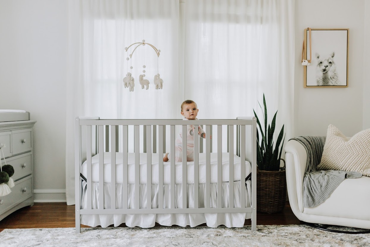 Baby in crib with decor mobile.